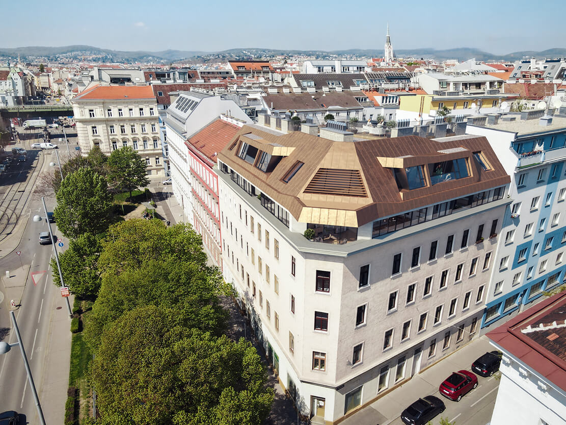 Luftaufnahme des Eckhauses Zimmermannplatz 6 mit neuem, bronzefarbenem Dachgeschoss und Blick über Wien